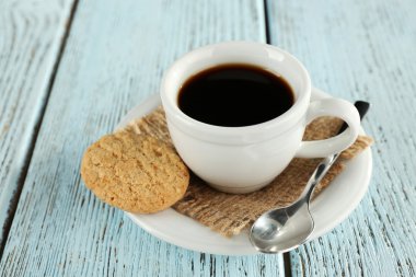 Cup of coffee with burlap cloth, spoon and cookies on color wooden background
