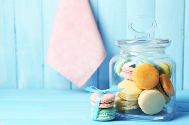 Gentle colorful macaroons in glass jar on color wooden table background