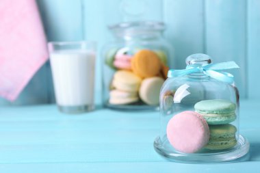 Gentle colorful macaroons in glass jell jar, milk glass and towel on color wooden table background