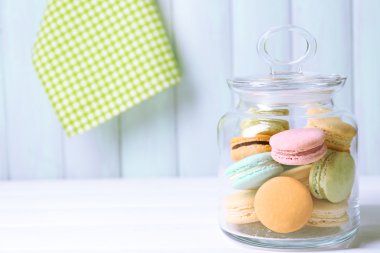 Gentle colorful macaroons in glass jar on color wooden table background