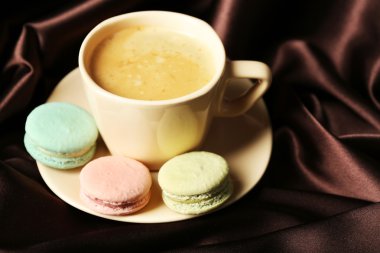 Gentle colorful macaroons and black coffee in mug on color fabric background