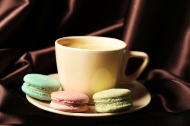Gentle colorful macaroons and black coffee in mug on color fabric background
