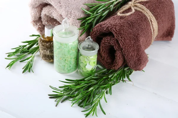 Branches of rosemary, towels and bottle with massage oil and sea salt on color wooden background. Rosemary spa concept — Stock Photo, Image