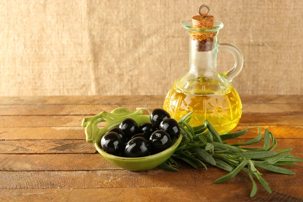 Black marinated olives in green saucepan with oil near branch and oilcan on rustic wooden background — Stock Photo, Image