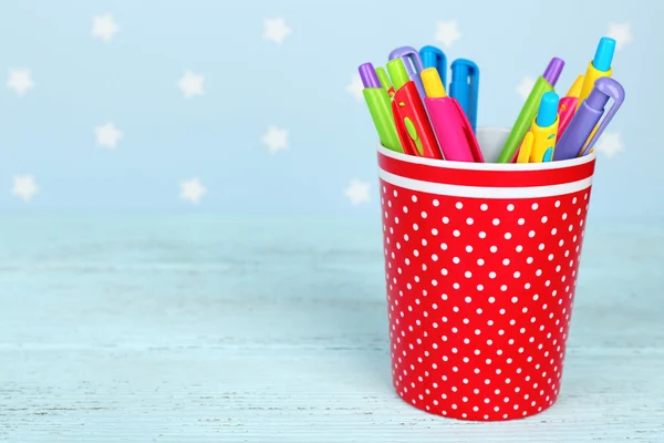 Plastic cup with different pens on color wooden table on color wooden table and blue background with printed stars — Stock Photo, Image