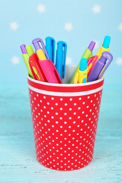 Plastic beker met verschillende pennen op de houten tafel kleur op kleur houten tafel en blauwe achtergrond met gedrukte sterren — Stockfoto