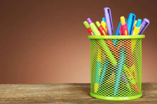 Stylos colorés en porte-métal vert sur table en bois et fond de couleur ombragé — Photo