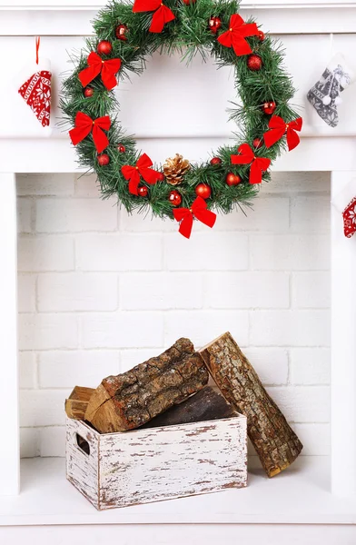 Fireplace with firewood and Christmas wreath on white wall background — Stock Photo, Image