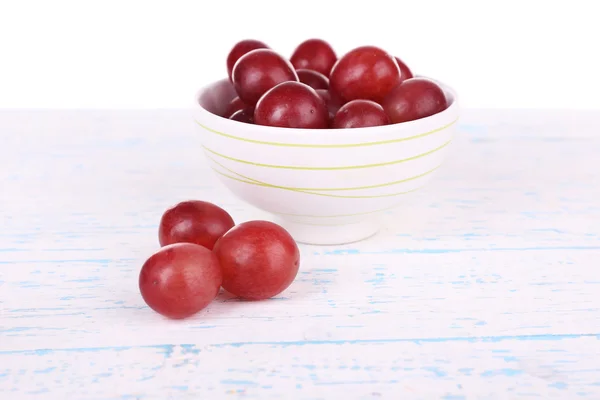 Tigela de uvas vermelhas na superfície de madeira de cor isolada no fundo branco — Fotografia de Stock