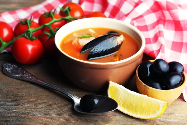 Tasty soup with shrimps, mussels, tomatoes and black olives in bowl on wooden background — Stock Photo, Image