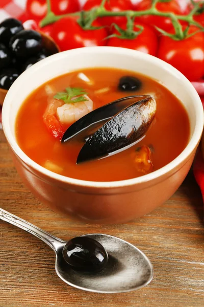 Tasty soup with shrimps, mussels, tomatoes and black olives in bowl on wooden background — Stock Photo, Image