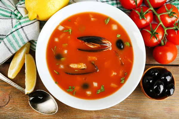 Tasty soup with mussels, tomatoes and black olives in bowl on wooden background — Stock Photo, Image