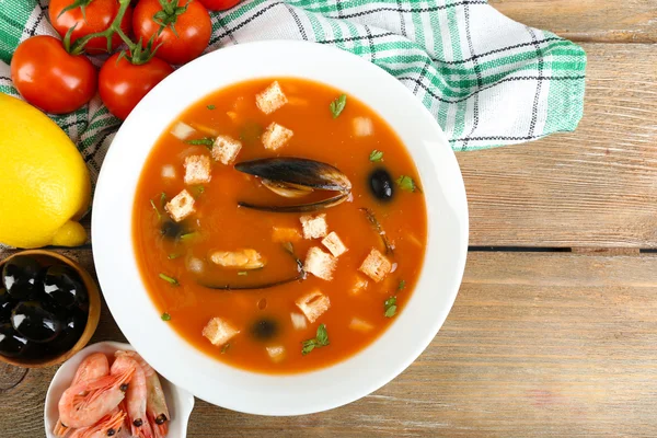 Tasty soup with mussels, tomatoes and black olives in bowl on wooden background — Stock Photo, Image