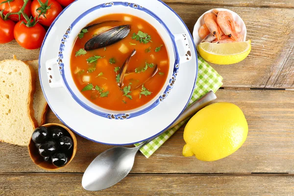 Sopa sabrosa con gambas, mejillones, tomates y aceitunas negras en un bol sobre fondo de madera — Foto de Stock