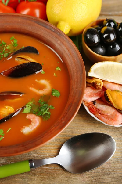 Tasty soup with shrimps, mussels, tomatoes and black olives in bowl on wooden background — Stock Photo, Image