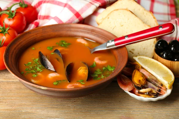 Tasty soup with shrimps, mussels, tomatoes and black olives in bowl on wooden background — Stock Photo, Image