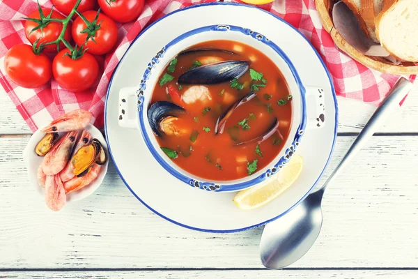 Tasty soup with shrimps, mussels, tomatoes and black olives in bowl on wooden background — Stock Photo, Image