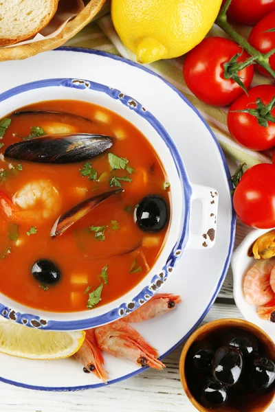 Tasty soup with shrimps, mussels, tomatoes and black olives in bowl on wooden background — Stock Photo, Image