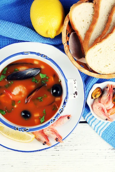 Tasty soup with shrimps, mussels, tomatoes and black olives in bowl on wooden background — Stock Photo, Image