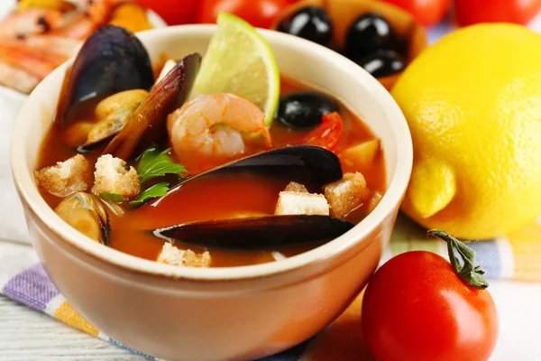 Tasty soup with shrimps, mussels, tomatoes and black olives in bowl on wooden background — Stock Photo, Image