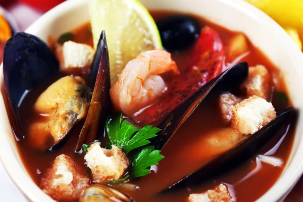 Вкусный суп с креветками, мидиями, помидорами и черными оливками в миске на деревянном фоне — стоковое фото