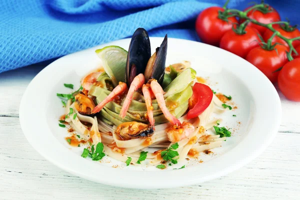 Leckere Pasta mit Garnelen, Miesmuscheln und Tomaten auf Teller auf Holzgrund — Stockfoto