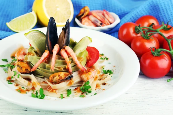 Chutné těstoviny s krevetami, mušle a rajčaty na štítku na dřevěné pozadí — Stock fotografie