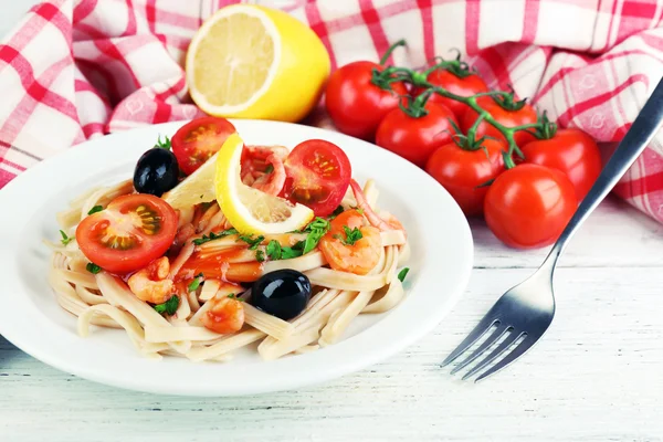 Smakelijke pasta met garnalen, zwarte olijven en tomatensaus op plaat op houten achtergrond — Stockfoto