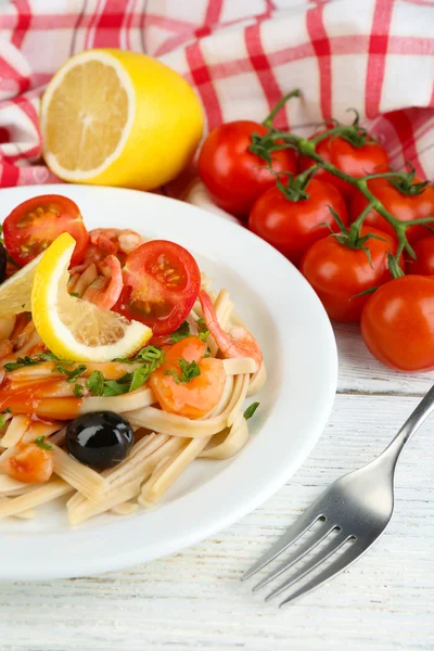 Tasty pasta with shrimps, black olives and tomato sauce on plate on wooden background — Stock Photo, Image