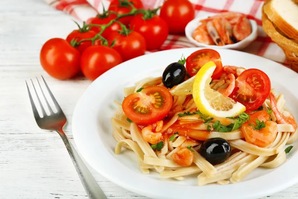 Pasta saporita con gamberetti, olive nere e salsa di pomodoro su piatto su fondo di legno — Foto Stock