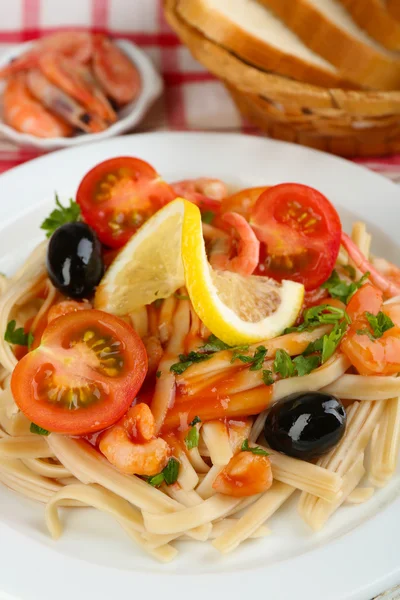 Tasty pasta with shrimps, black olives and tomato sauce on plate on wooden background — Stock Photo, Image