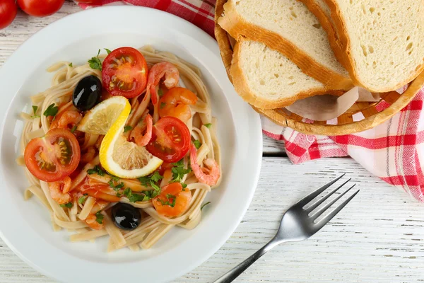 Tasty pasta with shrimps, black olives and tomato sauce on plate on wooden background — Stock Photo, Image