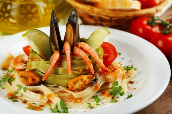 Tasty pasta with shrimps, mussels, tomatoes on plate on wooden background — Stock Photo, Image