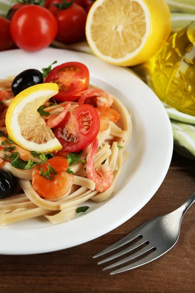 Tasty pasta with shrimps, mussels, black olives and tomato sauce on plate on wooden background — Stock Photo, Image