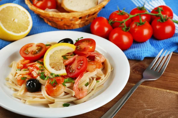 Leckere Pasta mit Garnelen, Miesmuscheln, schwarzen Oliven und Tomatensauce auf Teller auf Holzgrund — Stockfoto