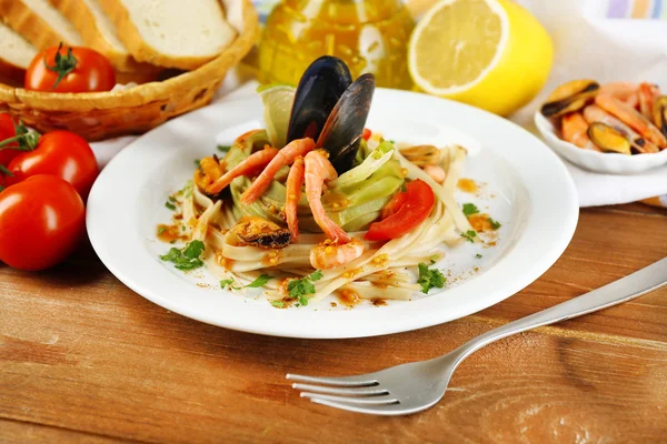Tasty pasta with shrimps, mussels, tomatoes on plate on wooden background — Stock Photo, Image