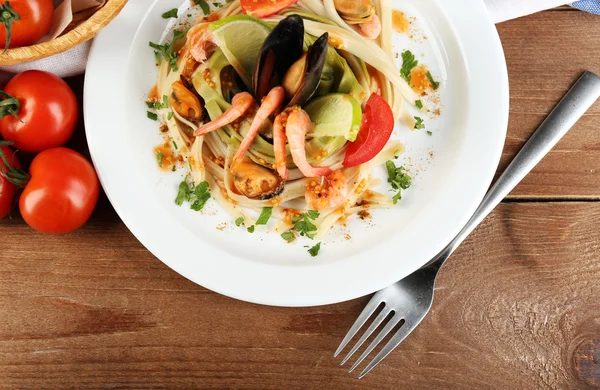 Leckere Pasta mit Garnelen, Miesmuscheln, Tomaten auf Teller auf Holzgrund — Stockfoto