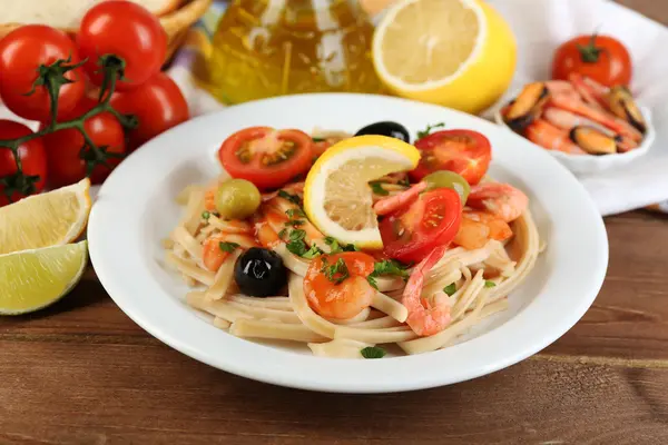 Leckere Pasta mit Garnelen, Miesmuscheln, schwarzen Oliven und Tomatensauce auf Teller auf Holzgrund — Stockfoto