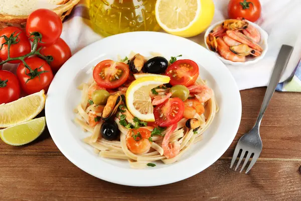 Smakelijke pasta met tomatensaus op plaat op houten achtergrond, garnalen, mosselen en zwarte olijven — Stockfoto