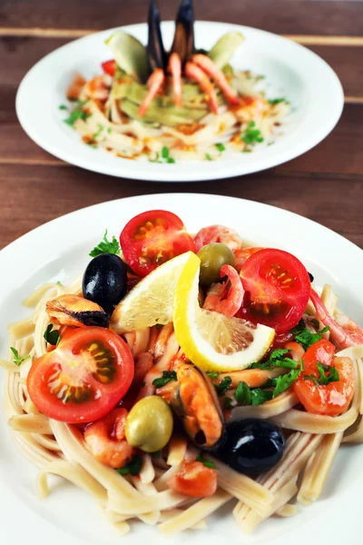 Auswahl an leckeren Nudeln mit Garnelen, Miesmuscheln, schwarzen Oliven und Tomatensauce auf Tellern auf Holzboden — Stockfoto