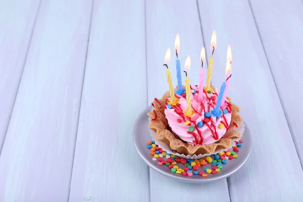 蛋糕杯碟上的蜡烛与色彩木制背景的闪光 — 图库照片