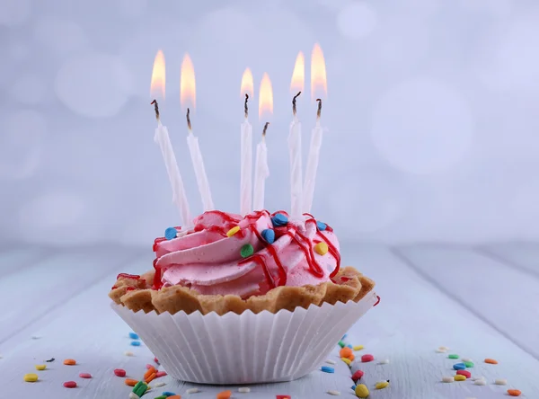 Cake van de kindverjaardag cup met kaarsen en sparkles op kleur houten tafel en lichte achtergrond — Stockfoto