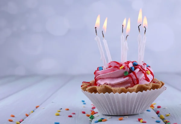 Birthday cup cake with candles and sparkles on color wooden table and light background — Stock Photo, Image