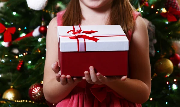 Little girl holding present box near Christmas tree on light background — Stock Photo, Image