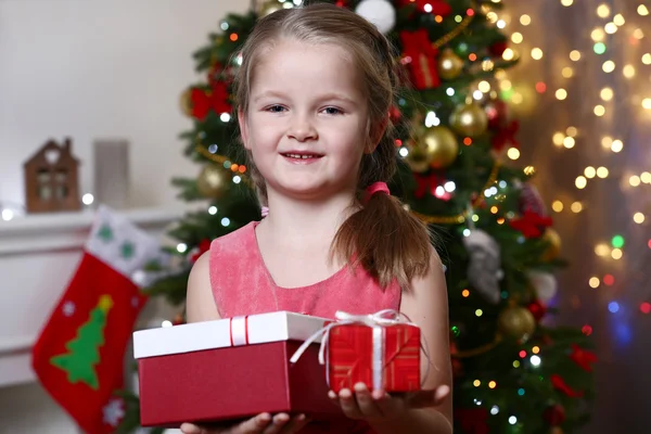 Little girl holding present boxes near Christmas tree on light background — Stockfoto