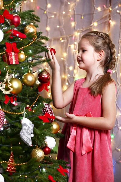 Little girl decorating Christmas tree on bright background — Stock Photo, Image