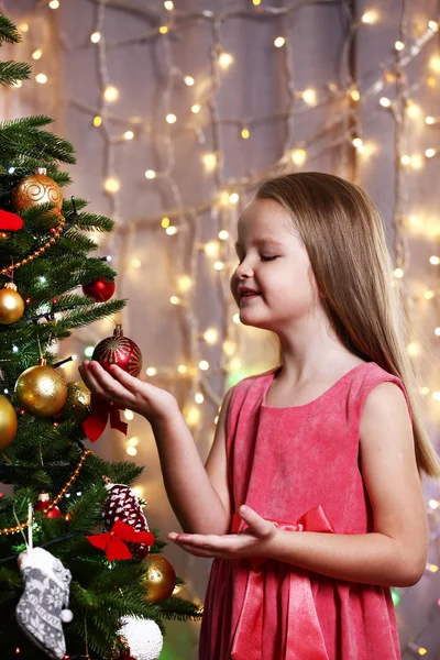 Parlak arka planda Noel ağacı süsleyen küçük kız. — Stok fotoğraf