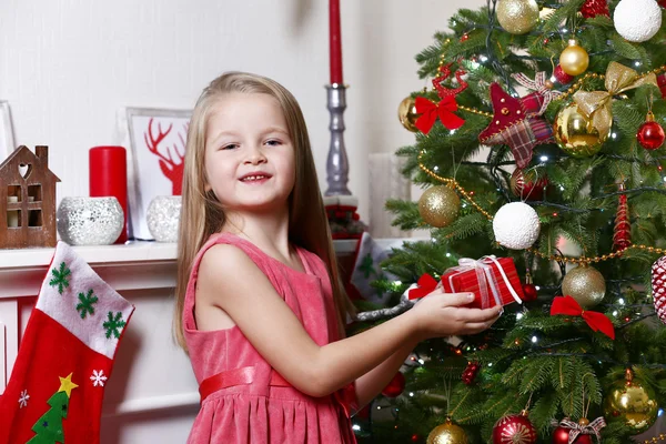 Little girl holding present box near fir tree on Christmas decoration background — Stok fotoğraf