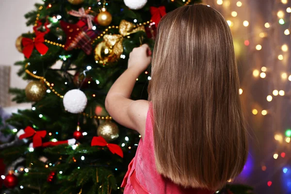 Little girl decorating Christmas tree on bright background — Stock Photo, Image
