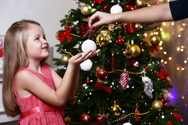 Little girl taking bauble near Christmas tree on white wall background — Zdjęcie stockowe